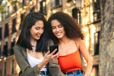İki genç bayan cep telefonundan bir şey izliyorlar.