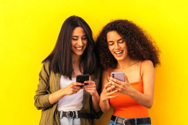 Afro ve beyaz kadınlar sarı duvara yaslanmış gezici kadınları izliyorlar.