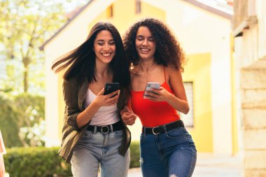 Kadınlar merdivenlerden çıkarken cep telefonlarını kullanarak gülüyorlar.