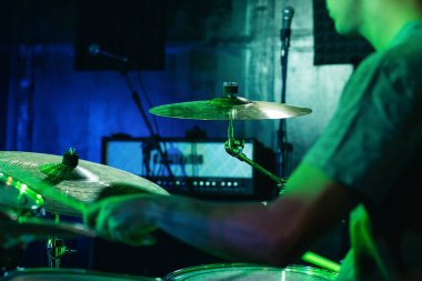 Genç müzisyen bir konserde davul çalıyor. Parlak, renkli ışıklar sahneyi aydınlatır ve sanatçının müziğe olan tutkusunu ön plana çıkarır.
