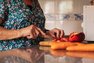 Gözlüklü yaşlı bir kadının evde lezzetli bir yemek hazırlarken yakın çekimi. Mutfakta kırmızı biber kesiyor.