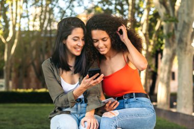 İki genç bayan cep telefonundan bir şey izliyorlar.