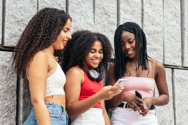 Üç afro saçlı Afro-Amerikalı kız akıllı telefon kullanıyor ve sosyal ağlardan onları eğlendiren görüntüler ve videolar izliyorlar.