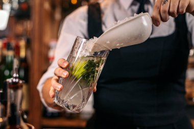 Tanınmayacak haldeki bir barmenin, uzun bir bardağa buz dökerek mojito hazırladığı yakın plan.