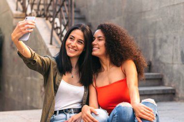 Merdivenlerde oturmuş selfie çeken iki güzel kadın.
