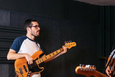 Bir müzik salonunda bas gitar çalan bir müzisyen. Sanatçı prova alanını dolduran derin ve yankı uyandıran notalar üretmeye odaklanır..