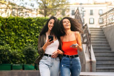 İki şık genç bayan yürüyor ve cep telefonlarını kullanıyor.