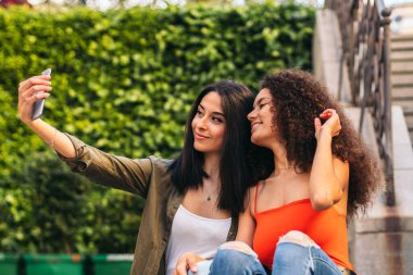 Merdivenlerde oturmuş selfie çeken iki güzel kadın.
