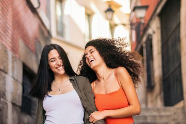 İki genç kadın merdivenlerden aşağı inerken gülümsüyor ellerini tutuyor ve sarılıyorlar.