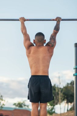 Bir erkek sporcunun barın önünde barfiks çekerken görüntüsü. jimnastik