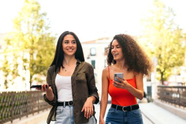 Yürüyen ve cep telefonunu kullanan iki genç kadın.