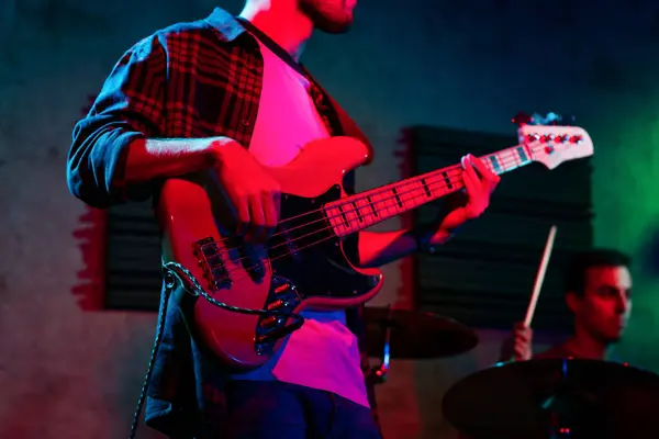 stock image Unrecognizable young man in casual clothes standing in an indoors stage and playing bass in real live concert