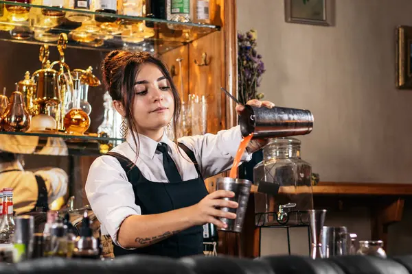 Genç bayan barmen bir gece barında kokteyl karıştırıcıyla kokteyl hazırlıyor.