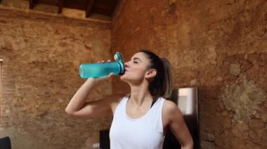 Spor giyimli kadın sporcu elleri kalçasında evde içme suyunun keyfini çıkarıyor.
