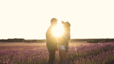 İçerikli adamın şapkalı nazik kız arkadaşını kucaklarken arka tarafta çiçek açan lavanta rengine karşı birbirine bakması.