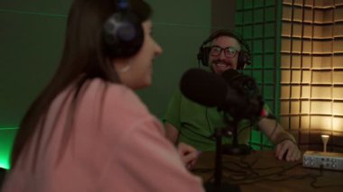Günlük kıyafetleri ve kulaklıkları içinde genç bir radyo sunucusu mikrofonla masada oturuyor ve stüdyoda podcast sırasında anonim bir meslektaşla iletişim kuruyor.