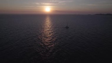 İspanya 'nın İbiza şehrinde gün batımında, dağlık bölgede sakin mavi denizde hızla yüzen motorlu teknenin muhteşem insansız hava aracı görüntüsünden.
