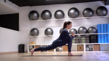 Yoga yapan ve poz veren sağlıklı genç bir kadının yan görüntüsü Crescent Lunge ve üç bacaklı aşağı bakan köpek ve fitness stüdyosundaki yarım güvercin pozisyonları da dahil olmak üzere.
