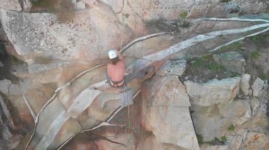 Sprey boyalı bir boyacı yukarıdan ipe asılı grafiti yapıyor kayalık yamaçta.