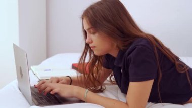 Evde uzak bir proje üzerinde çalışırken gündelik giysiler içinde yatıp dizüstü bilgisayarda yazan pozitif genç bir bayan serbest yazar.