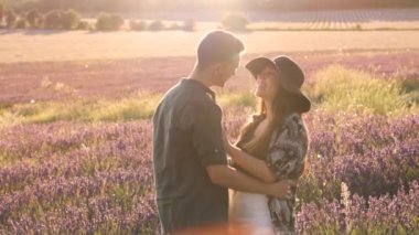 İçerikli adamın şapkalı nazik kız arkadaşını kucaklarken arka tarafta çiçek açan lavanta rengine karşı birbirine bakması.