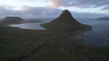 İzlanda 'da bulutlu gün batımına karşı durgun denizin yakınında yer alan Kirkjufell Dağı' nın insansız hava aracı görüntüsü