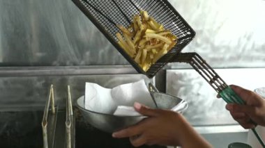 Fast food restoranının mutfağında yemek pişirirken taze patates kızartması dolduran isimsiz bir aşçı.