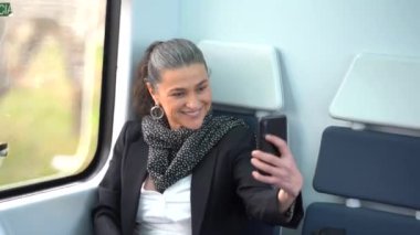 Eşarplı, cep telefonuyla fotoğraf çeken orta yaşlı bir kadın. Yolculuk sırasında yolcu koltuğunda, arabanın penceresinin yanında oturuyor.