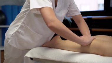 Klinikteki fizyoterapi seansında, beyaz cüppeli, tanınmayan bir masöz, tarladan çıkmış kadın bir hastaya masaj yapıyor.