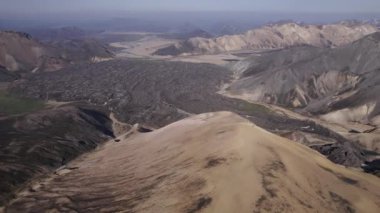 İzlanda 'nın dağlık kesimlerinde sabah vakti bulutlu mavi gökyüzüne karşı yürüyüşçülerle görkemli dağların insansız hava aracı görüntüsü.