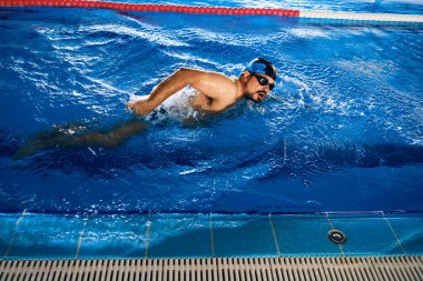 High angle of fit male swimming in crawl style in pool during training clipart