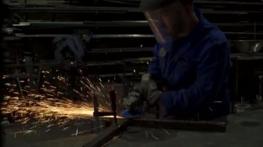 Eldiven ve üniformalı yüzsüz işçi fabrika inşaatlarının yanındaki masada metal kaynakçılığı yapıyor.