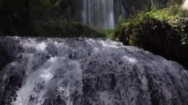 Güneşli bir günde ağaçların altındaki şelaleden