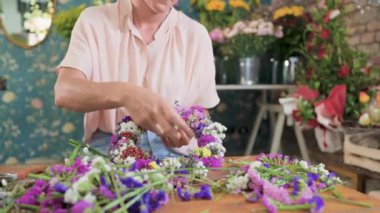 Kimliği belirsiz kadın çiçekçi dükkanda çalışırken taze renkli çiçeklerden çelenk yapıyor.
