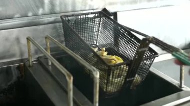 Kimliği belirsiz aşçı fast food restoranında patates kızartması pişirirken kızgın tavaya çiğ patates koyuyor.