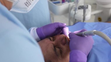 Kadın stomatolog, erkek hastanın dişlerini hastanede üniformalı iş arkadaşına karşı tedavi ediyor.