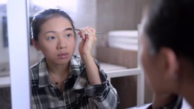 Makyaj yaparken ve aynaya bakarken kaş fırçalayan çekici etnik kadın.