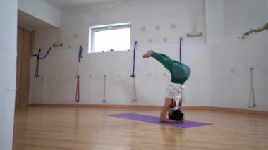 Spor kıyafetli esnek bir kadının evde yoga yaparken bacaklarını kaldırmış kafasının üstünde duruşu.