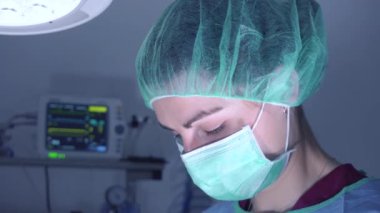 Ameliyathanede parlak ışık altında dururken profesyonel aletler kullanan tıbbi üniformalı bir kadın.