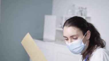 Koruyucu yüz maskesi takmış, elinde dosya kağıdıyla kadın doktor salgın sırasında birbirine bakarken hastanede kimliği belirsiz yaşlı bir kadınla konuşuyor.