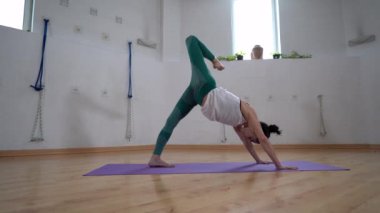 Üç Ayaklı Aşağı Yüzlü Köpek 'in minder üzerinde yoga yaparken dizinden alınına poz verdiğini gösteren olgun bir kadın.