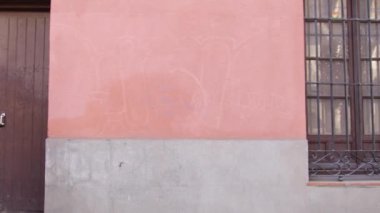 Şık giyinmiş, cep telefonlu mutlu siyah bir erkek şehir binasına karşı fayanslı yolda yürüyor.