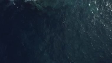 Güneşli bir günde mavi denizi ve kayalık uçurumu gösteren nefes kesici bir dron görüntüsü.