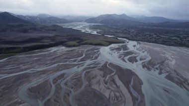 Güneşli bir günde İzlanda 'da, dağ sırtı yakınlarındaki yeşil vadide akan nehrin insansız hava aracı görüntüsünü yakınlaştır..