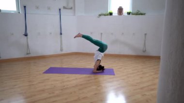 Spor kıyafetli esnek bir kadının evde yoga yaparken bacaklarını kaldırmış kafasının üstünde duruşu.