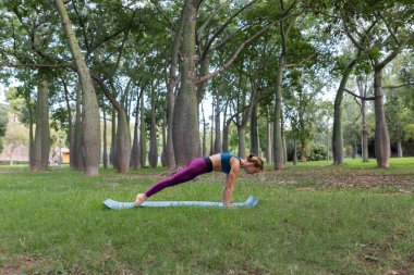 Aktif kıyafetli zayıf bir kadının gündüz vakti yoga minderinde Phalakasana performansı.