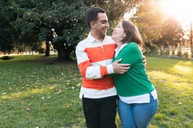 Gün batımında parkta kucaklaşıp gülümseyen genç Latin çift.