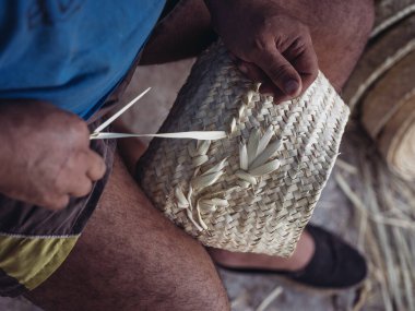 Palmito iplikçiklerinden narin bir sepet ören bir zanaatkarın detaylı yakın çekimi, karmaşık el işi ve geleneksel zanaat becerileri.