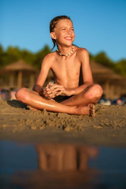 Deniz kenarında deniz kenarında deniz kenarında deniz kenarında oturan ve yaz tatili boyunca bakışlarını kaçıran kabuklu kolye takan sırılsıklam sırılsıklam bir çocuk.