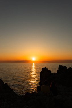 Dağların ve dalgalı denizin manzarası. Bulutlu gökyüzünün altında gece parlayan güneşle birlikte.